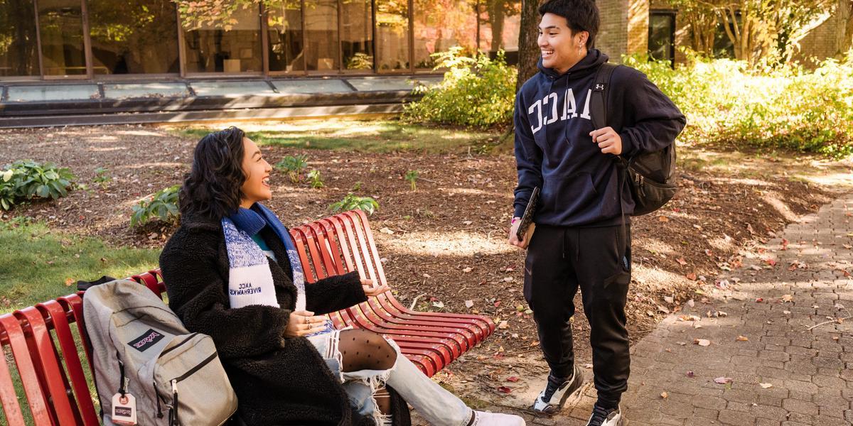 One student standing and talking to student at bench.